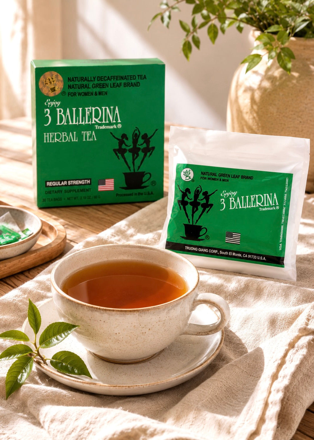 A cup of herbal tea on a saucer with a box and single-serve packet of Tiffly 3 Ballerina Herbal Tea in a warm, sunlit kitchen setting.
