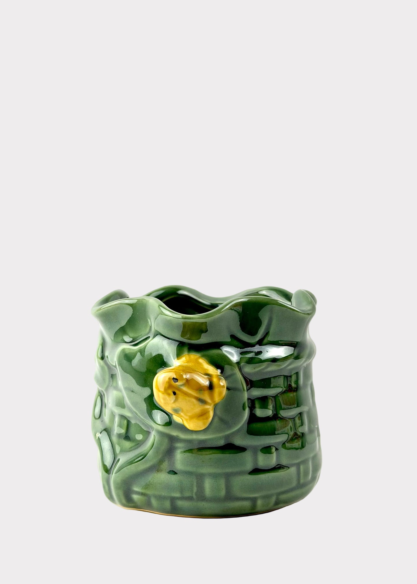 A green glazed ceramic planter shaped like a textured brick wall with a small yellow flower accent on the front, set against a plain white background.