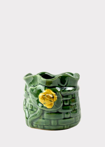 A green glazed ceramic planter shaped like a textured brick wall with a small yellow flower accent on the front, set against a plain white background.