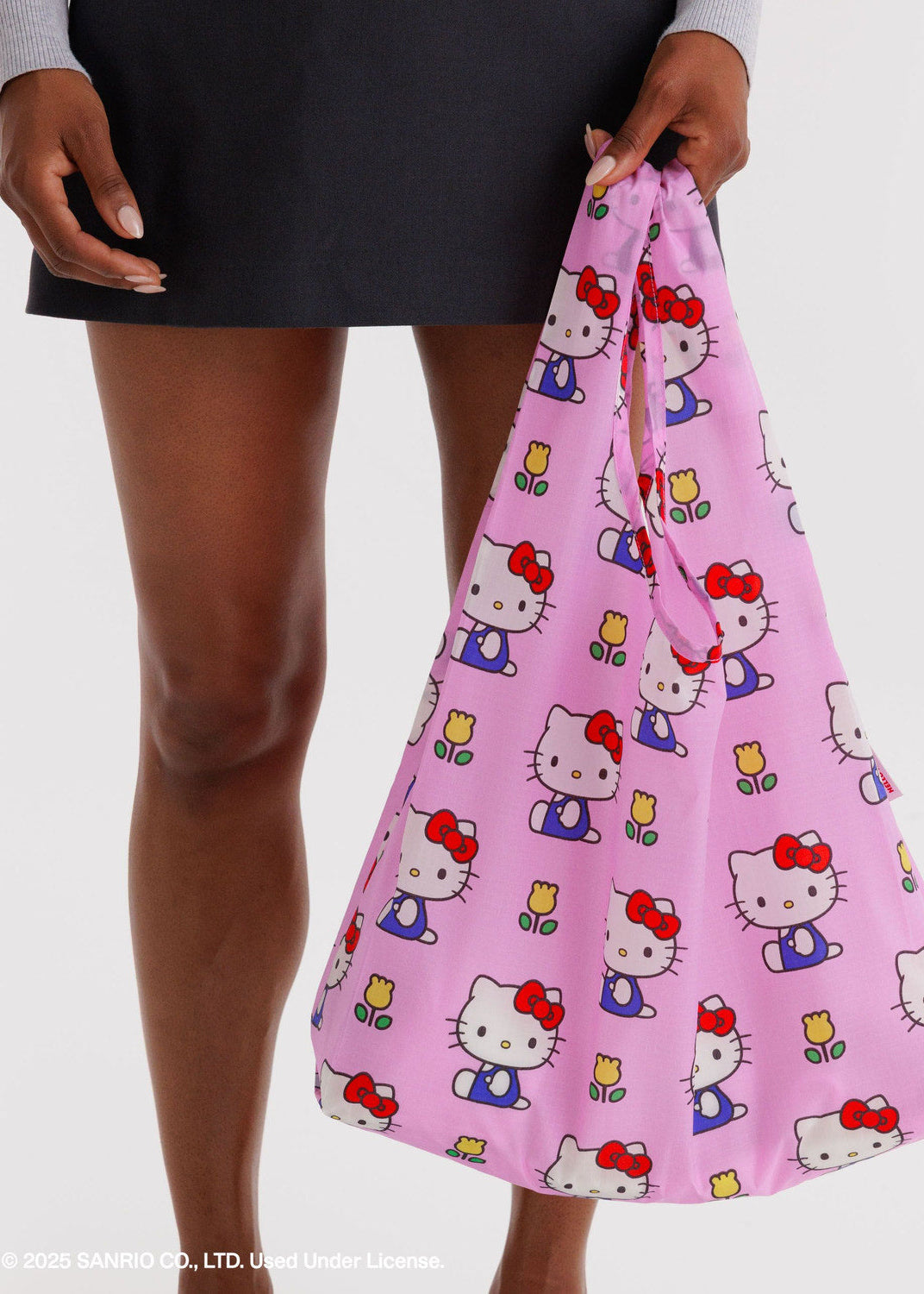 Pink reusable bag with Hello Kitty pattern held by a person against a white background