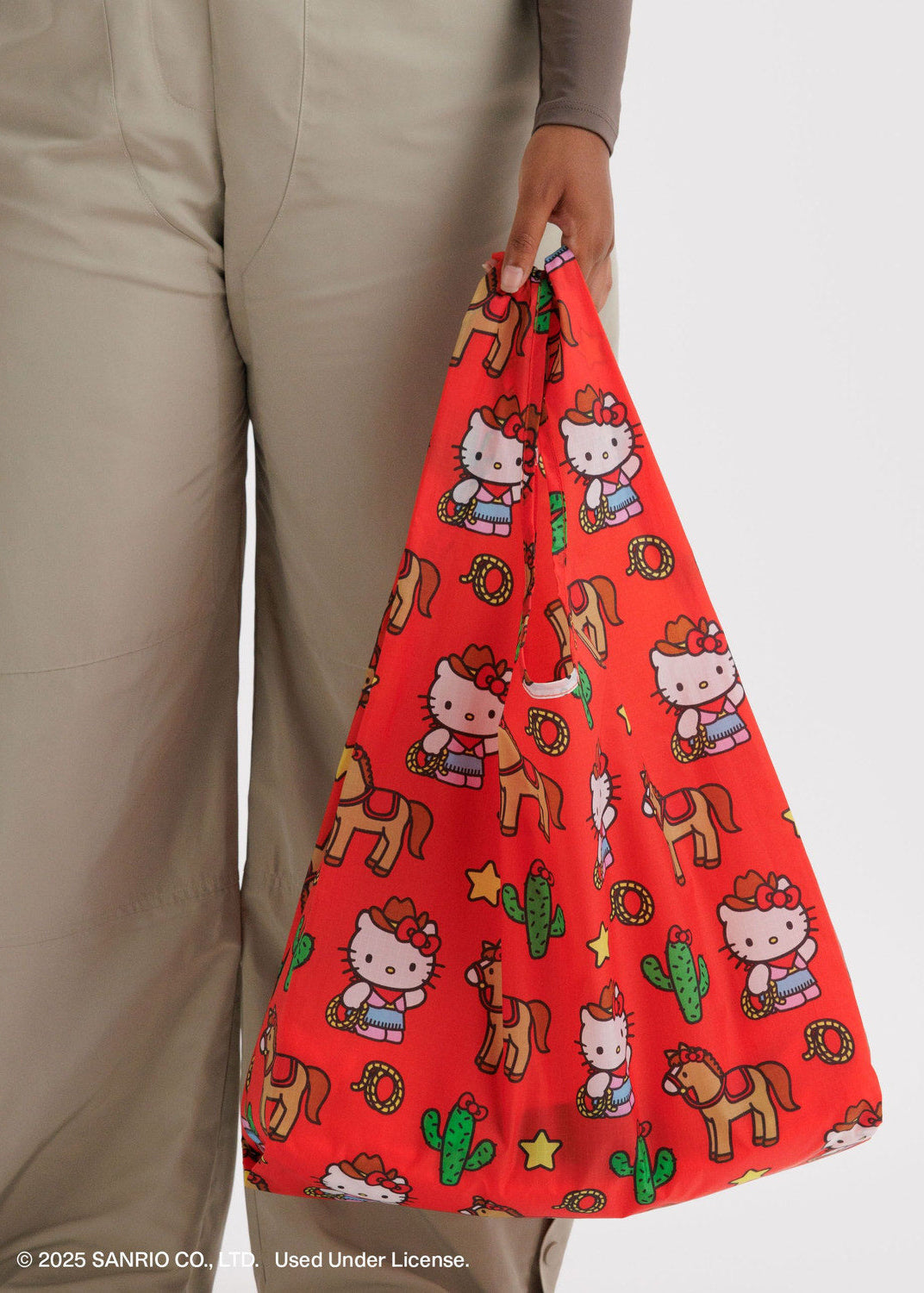 Red bag with Hello Kitty and horse pattern held by a person wearing beige pants.