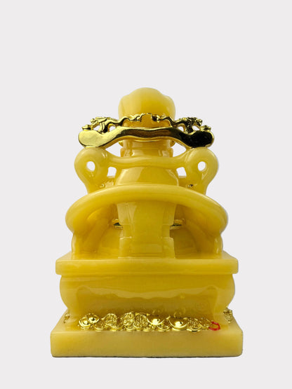 A yellow stone Buddha statue with gold-colored decorative accents on the head, hands, and base, shown against a plain light gray background.