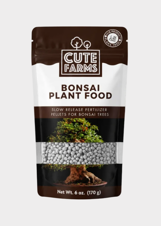 A 6 oz stand-up pouch of Cute Farms Bonsai Plant Food slow-release fertilizer pellets, shown next to a potted bonsai tree on a clean white background.