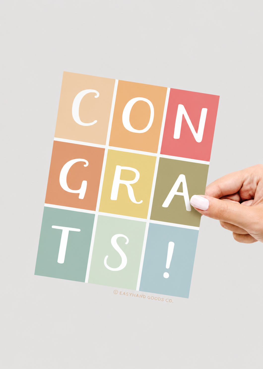 Hand holding a colorful 'CONGRATS!' card against a light gray background