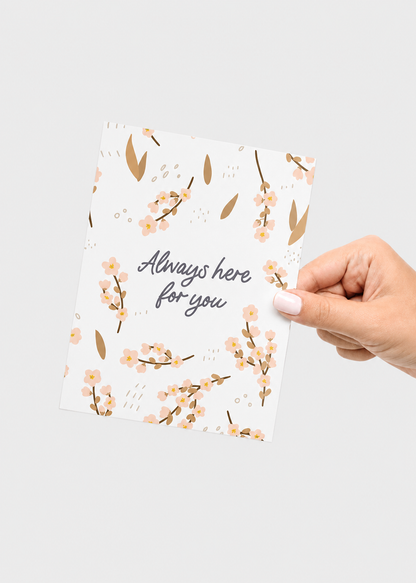 Hand holding a floral card with 'Always here for you' text on a light gray background