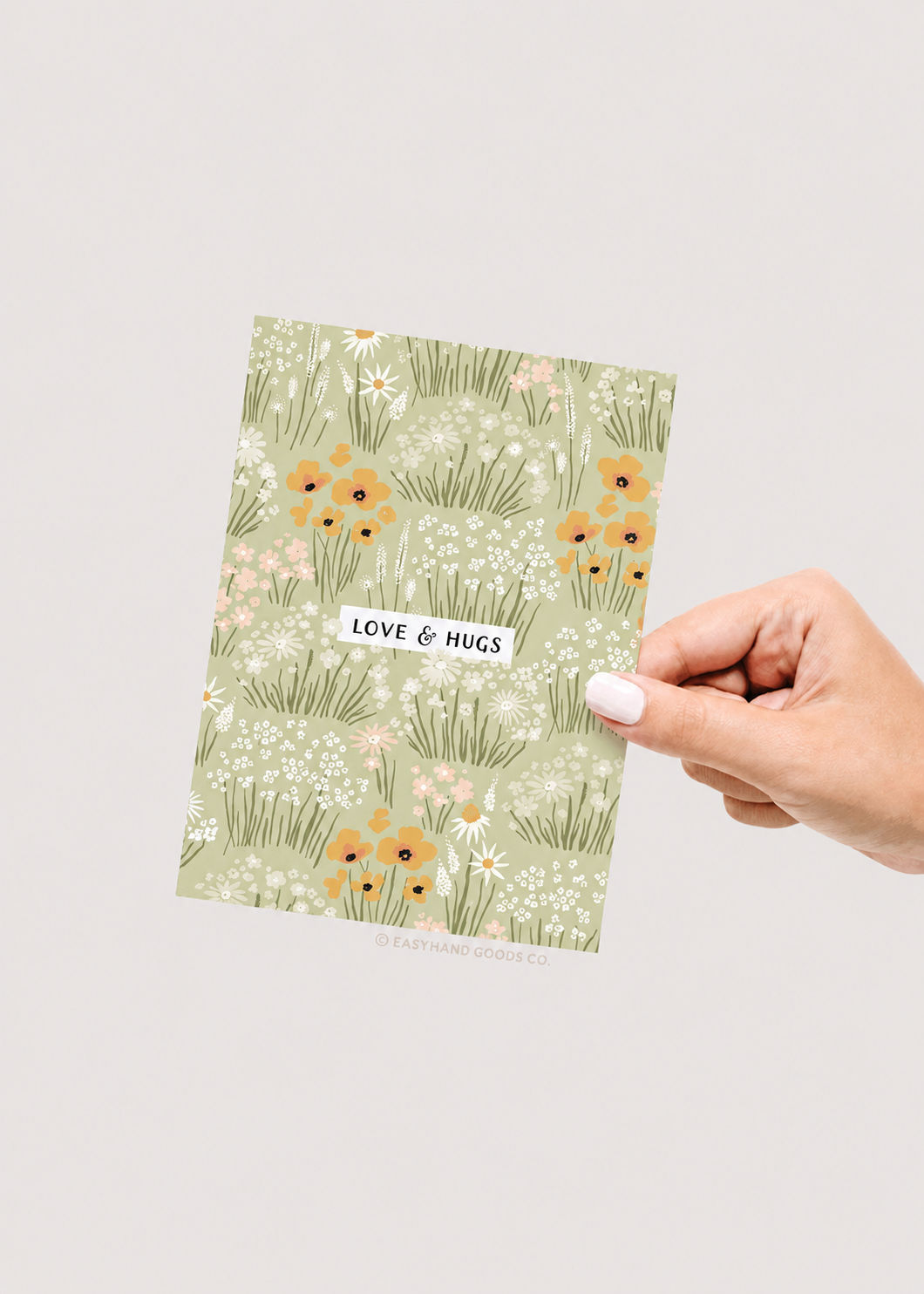 Hand holding a card with floral design and 'Love & Hugs' text on a light gray background