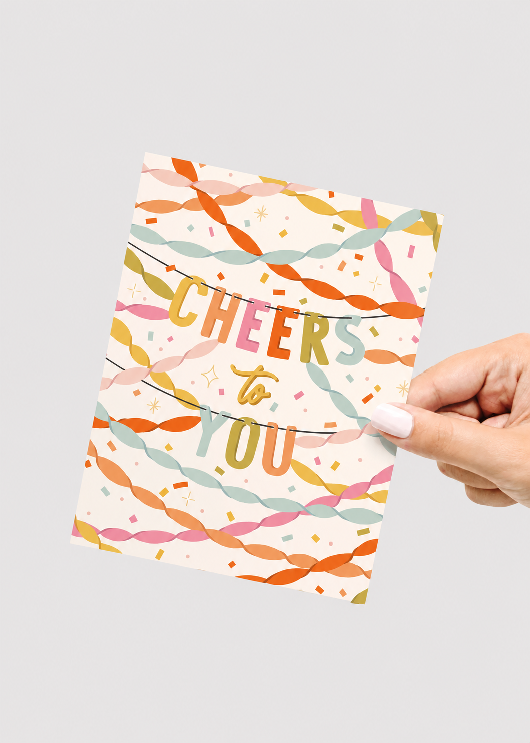 Hand holding a colorful card with 'Cheers to You' text on a light gray background