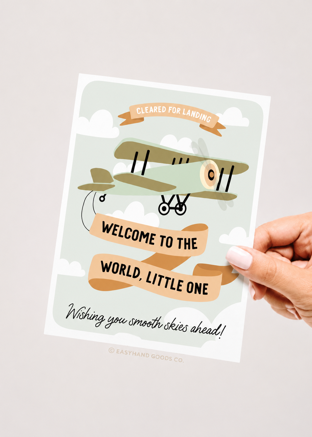 Newborn baby shower card with airplane illustration and text, held by a hand on a light background