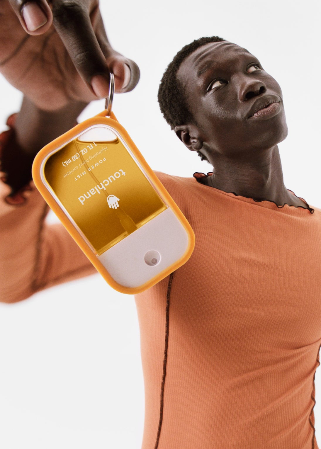 Person wearing an orange long-sleeve shirt with a close-up of a hand sanitizer  on their chest.
