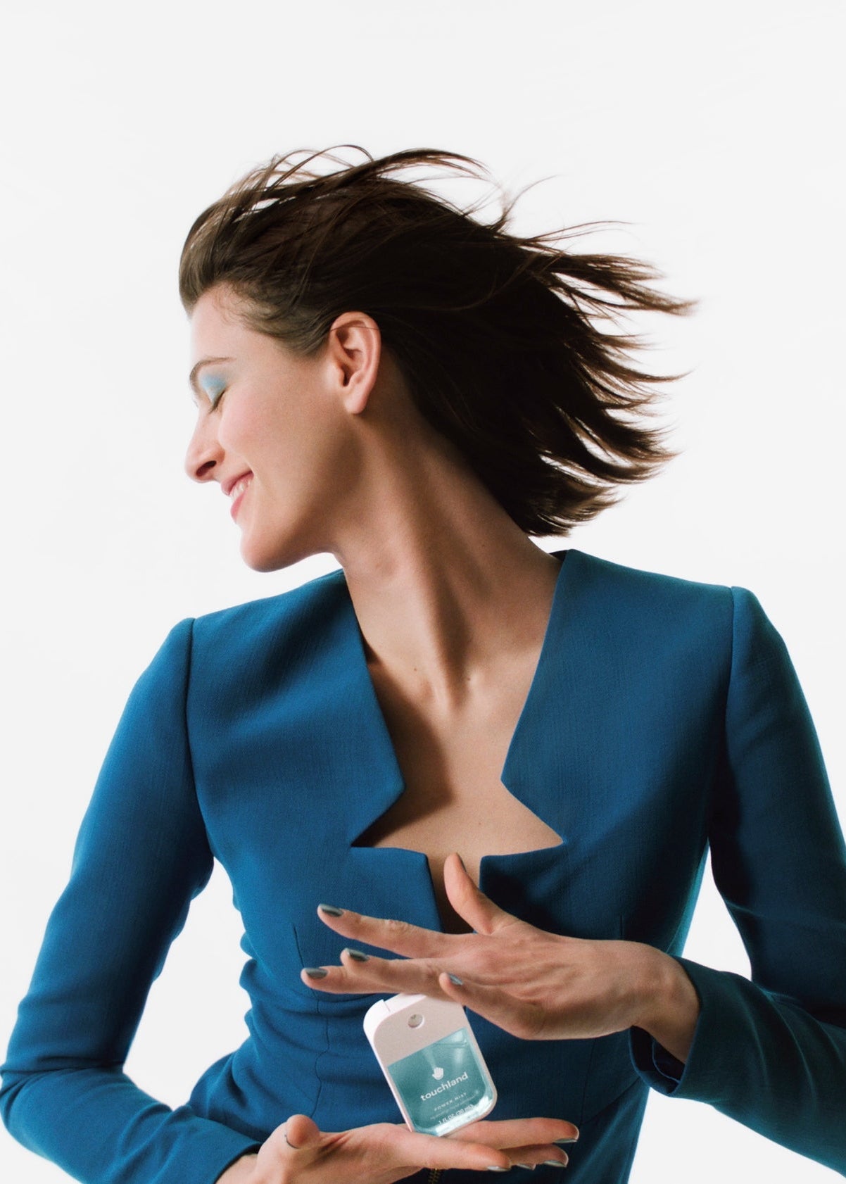 Woman in a blue suit holding a small bottle with a white label against a light gray background