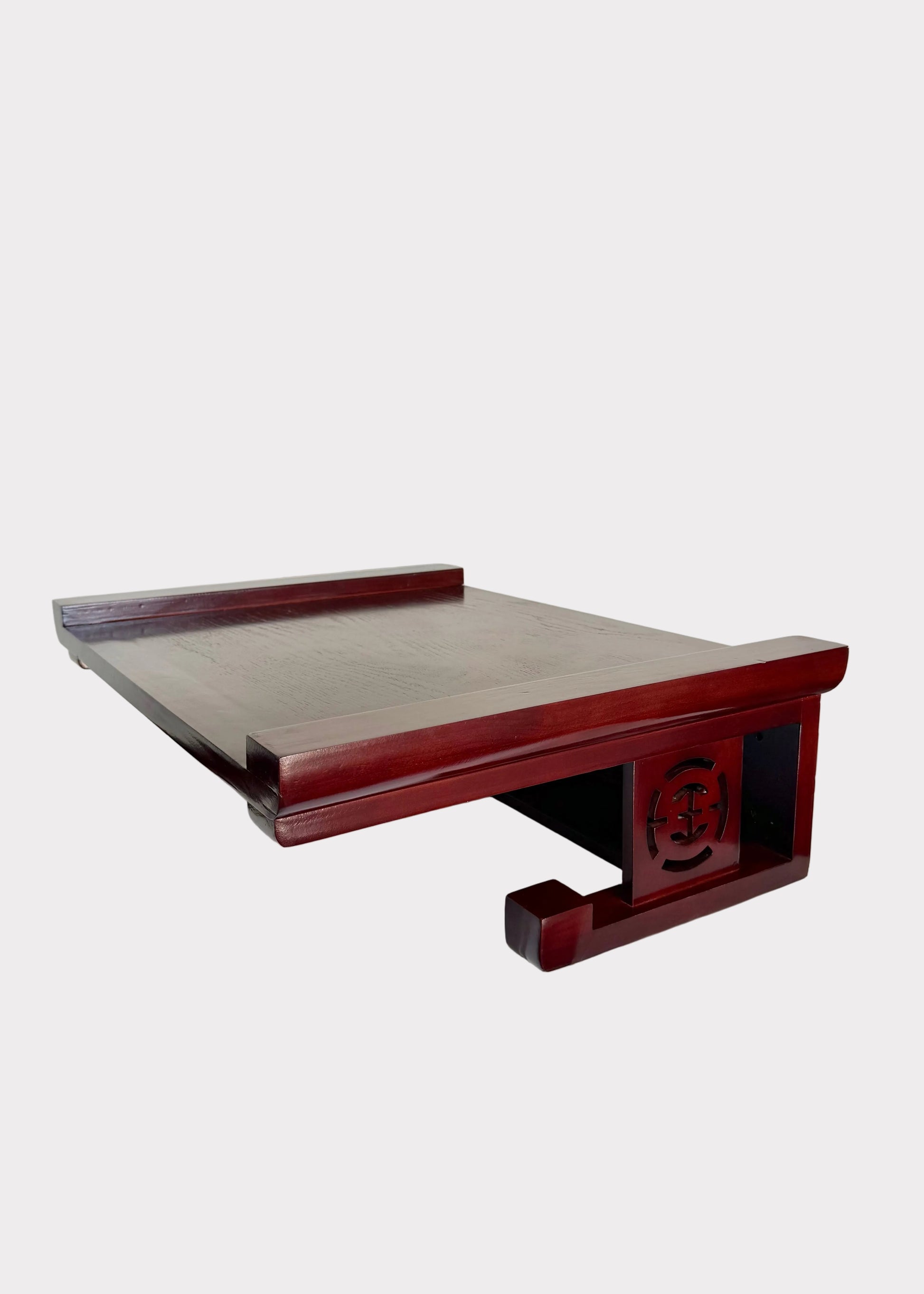 A dark reddish-brown wooden desk organizer or shelf with a slatted top and decorative carved side panel, shown resting on a white surface against a plain light wall.