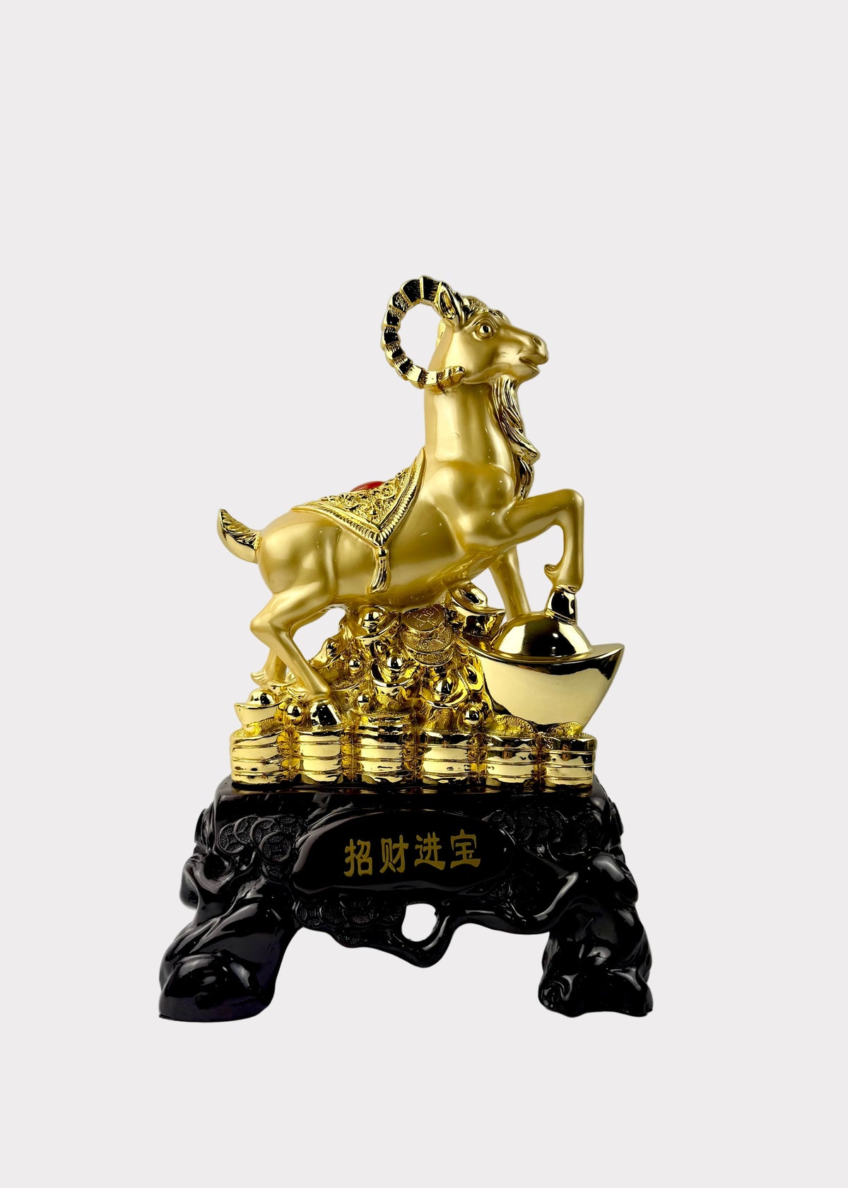 A golden ram figurine standing on a pile of gold ingots and coins, mounted on a black decorative base with Chinese characters, photographed against a plain light gray wall.