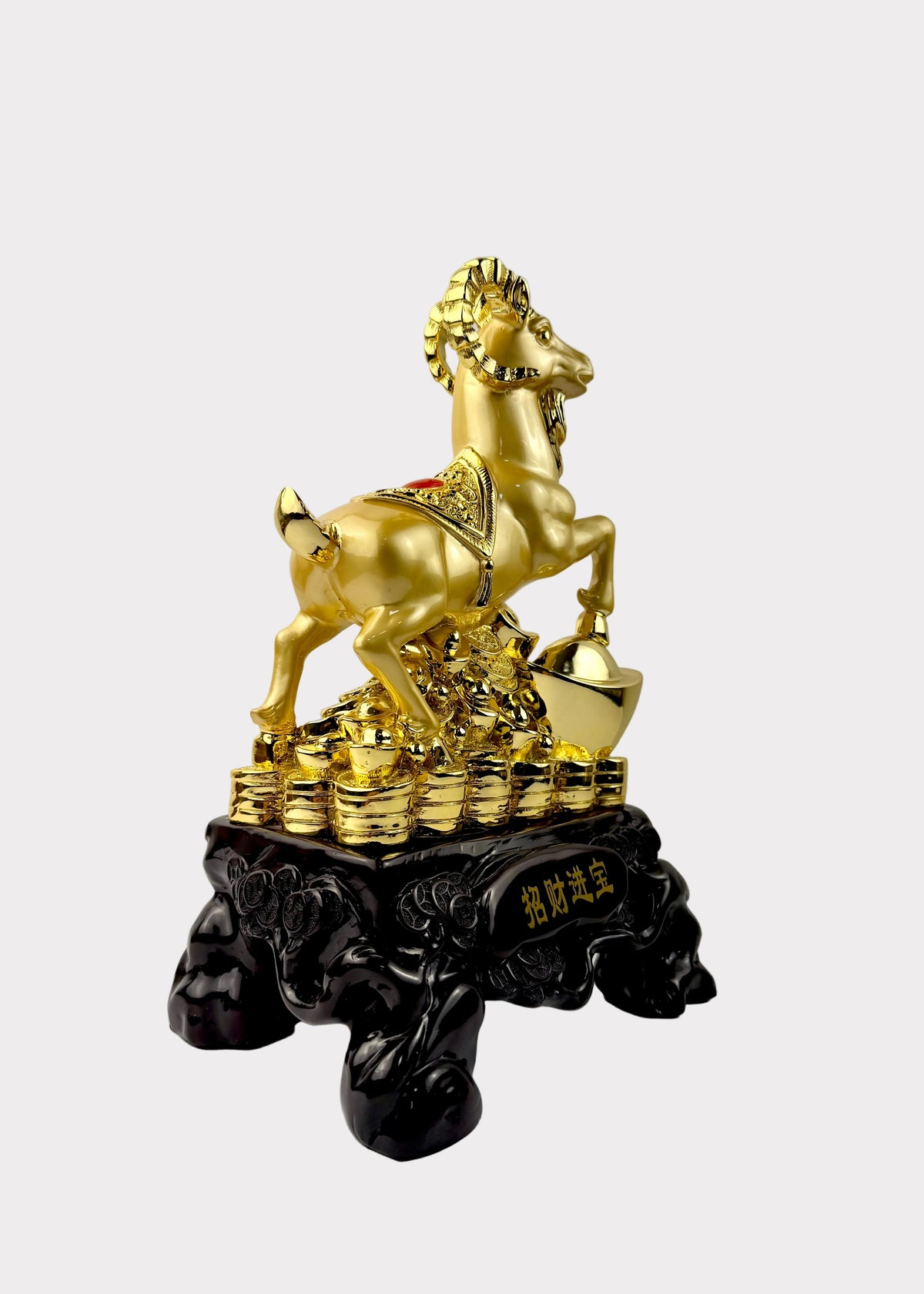 A golden ram figurine standing on a pile of gold coins, mounted on a black ornate base with Chinese characters, photographed against a plain light gray wall.