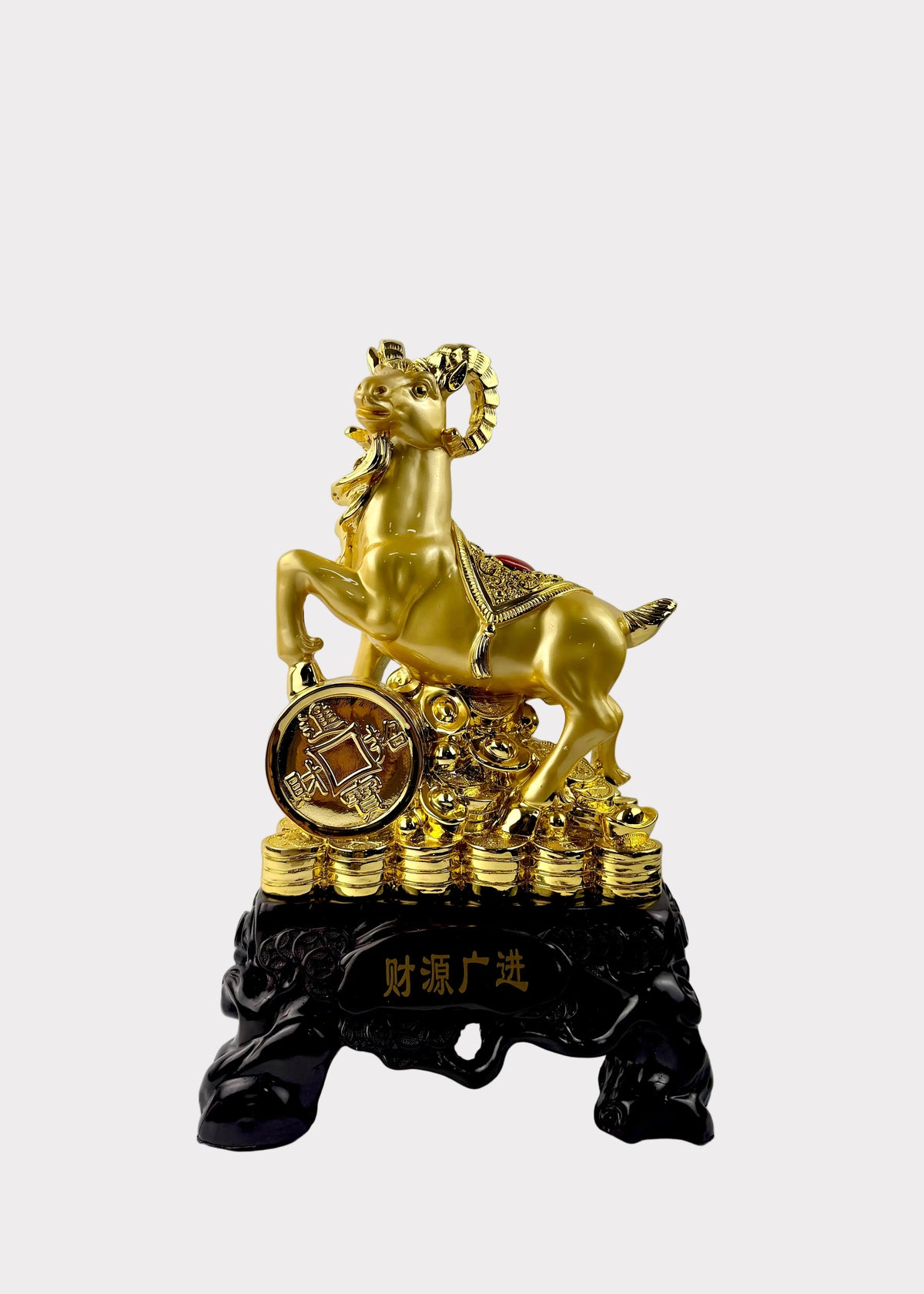 A golden ram figurine standing on a stack of gold coins, mounted on a black base with Chinese characters, photographed against a plain light gray wall and white surface.