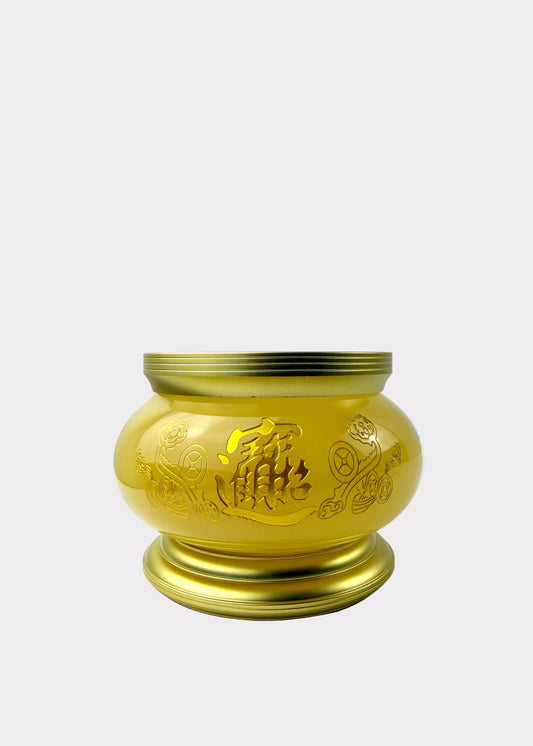 A shiny gold-colored metal incense burner with engraved Chinese characters and floral patterns, sitting on a white surface against a white wall.