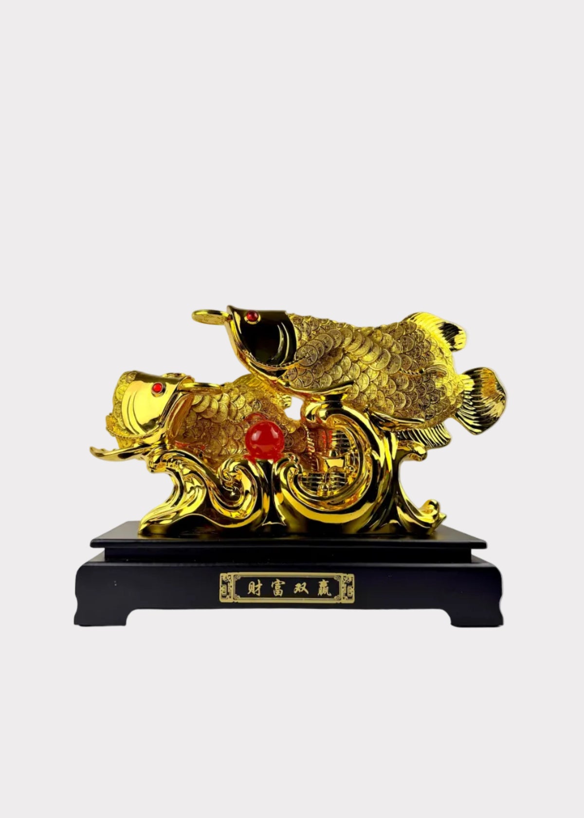 A golden Chinese fish sculpture on a black base with Chinese characters, set against a plain indoor wall.