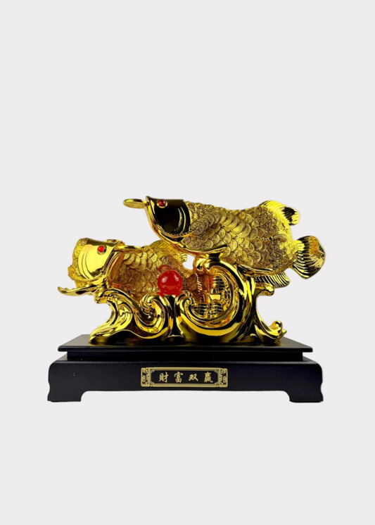 A golden Chinese fish sculpture on a black base with Chinese characters, set against a plain indoor wall.