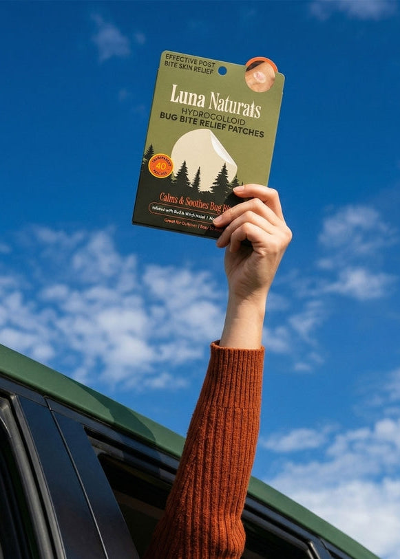 Person holding a package of Luna Naturals bug bite relief patches against a blue sky.