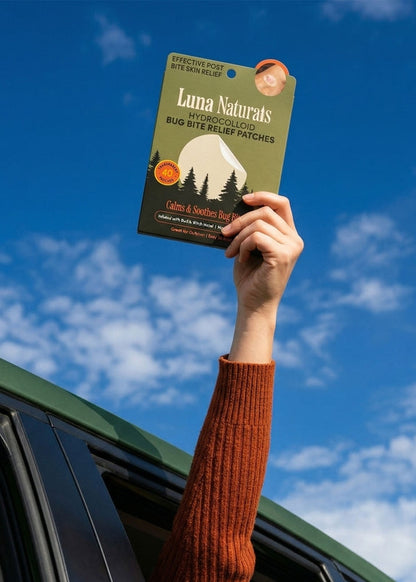 Person holding a package of Luna Naturals bug bite relief patches against a blue sky.