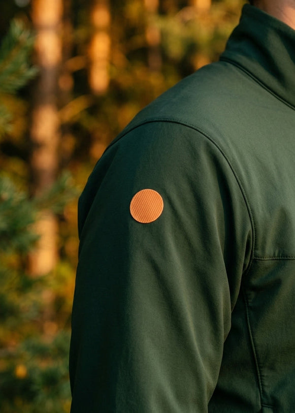 Green jacket with a brown patch on an arm against a blurred forest background