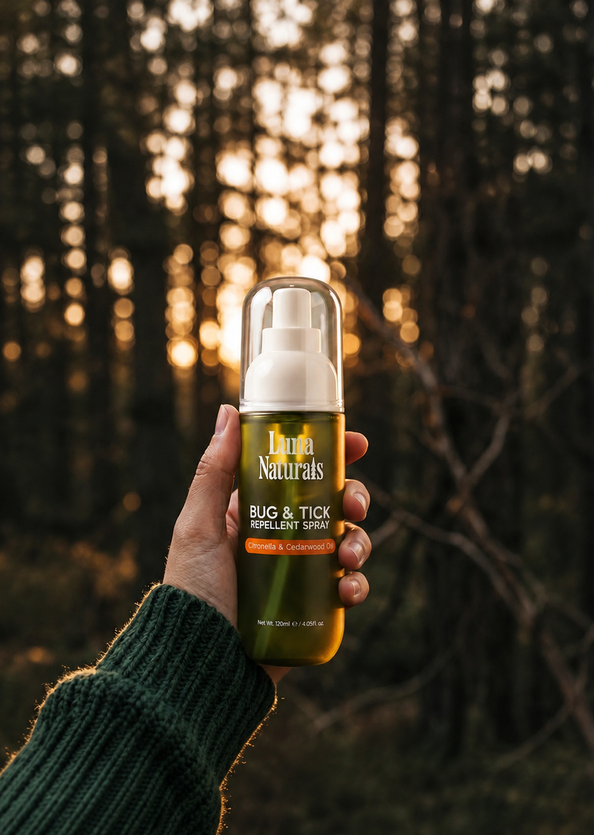 Hand holding a bottle of Naturals bug and tick repellent spray against a forest background.