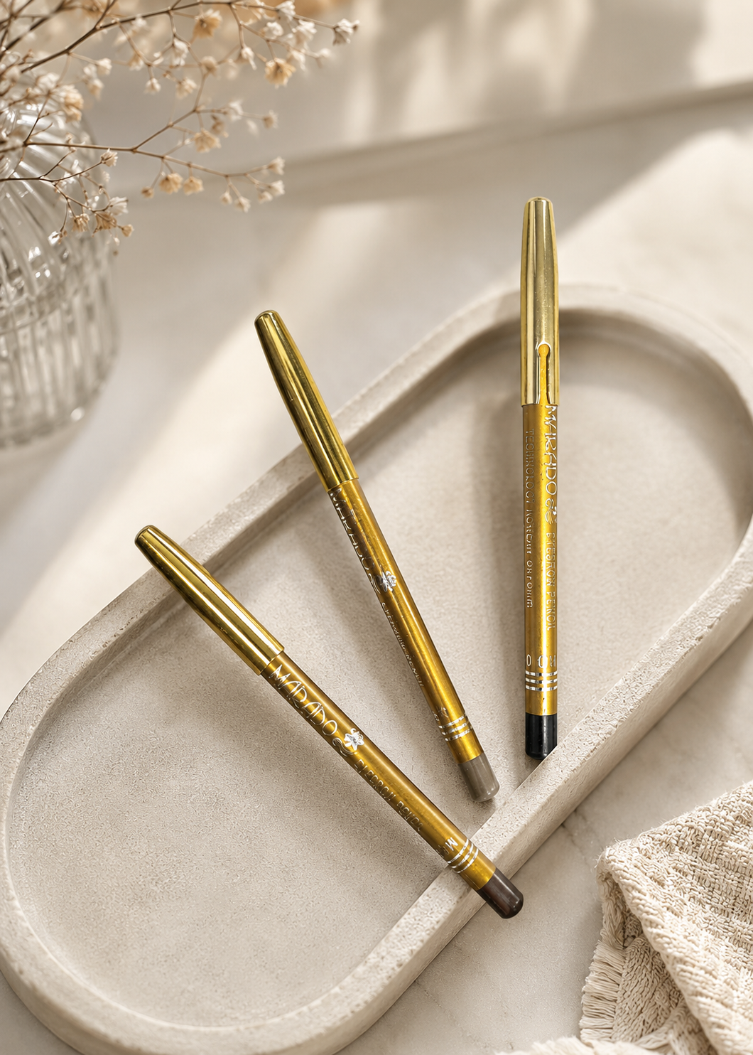 Three gold pens on a beige tray with a neutral background