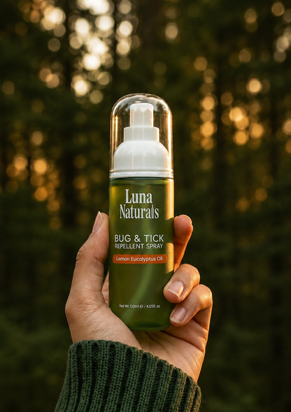 Hand holding Luna Naturals bug & tick repellent spray against a blurred natural background