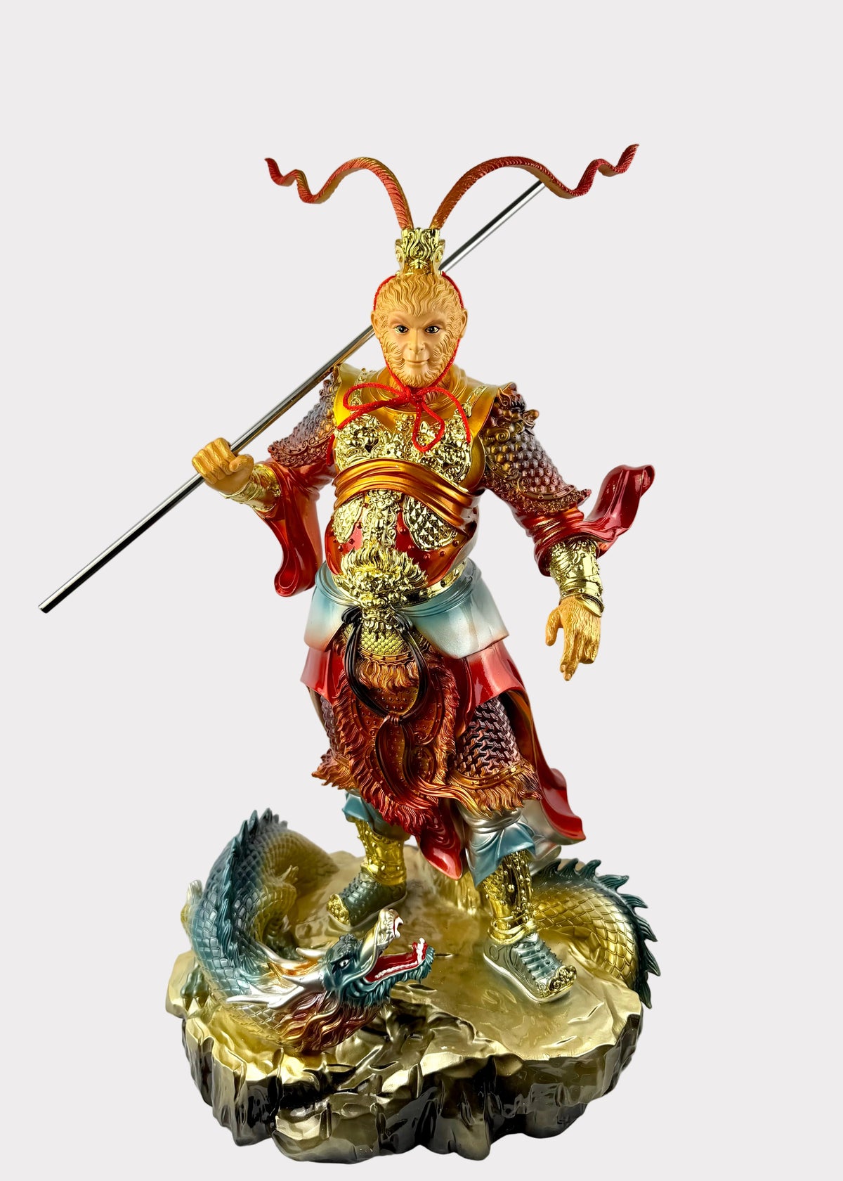 A detailed figurine of the Chinese deity Huang Sanyang (Monkey King) standing on a rocky base with a dragon, holding a golden staff. The figurine is highly detailed with gold, red, and blue colors, set against a plain white background.