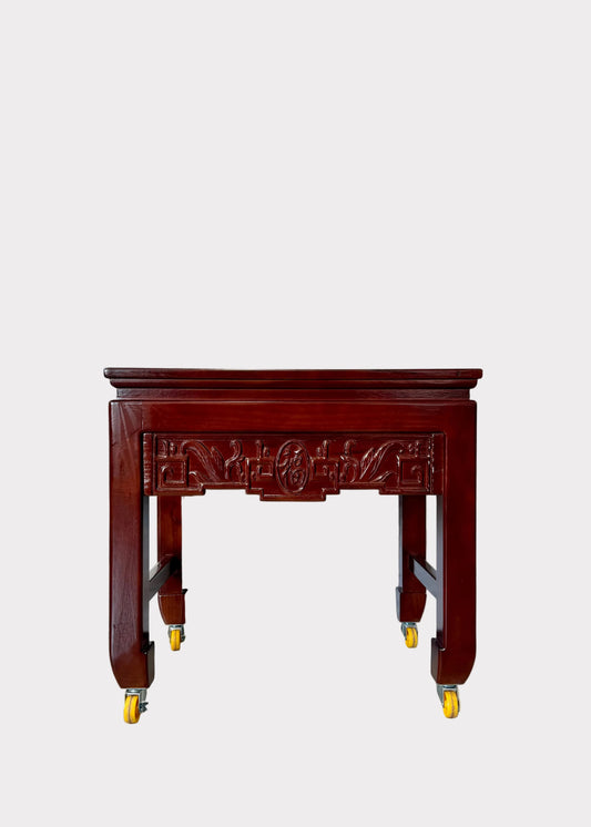 A dark reddish-brown carved wooden display table on casters, set against a white marble-patterned backdrop inside a retail store aisle.