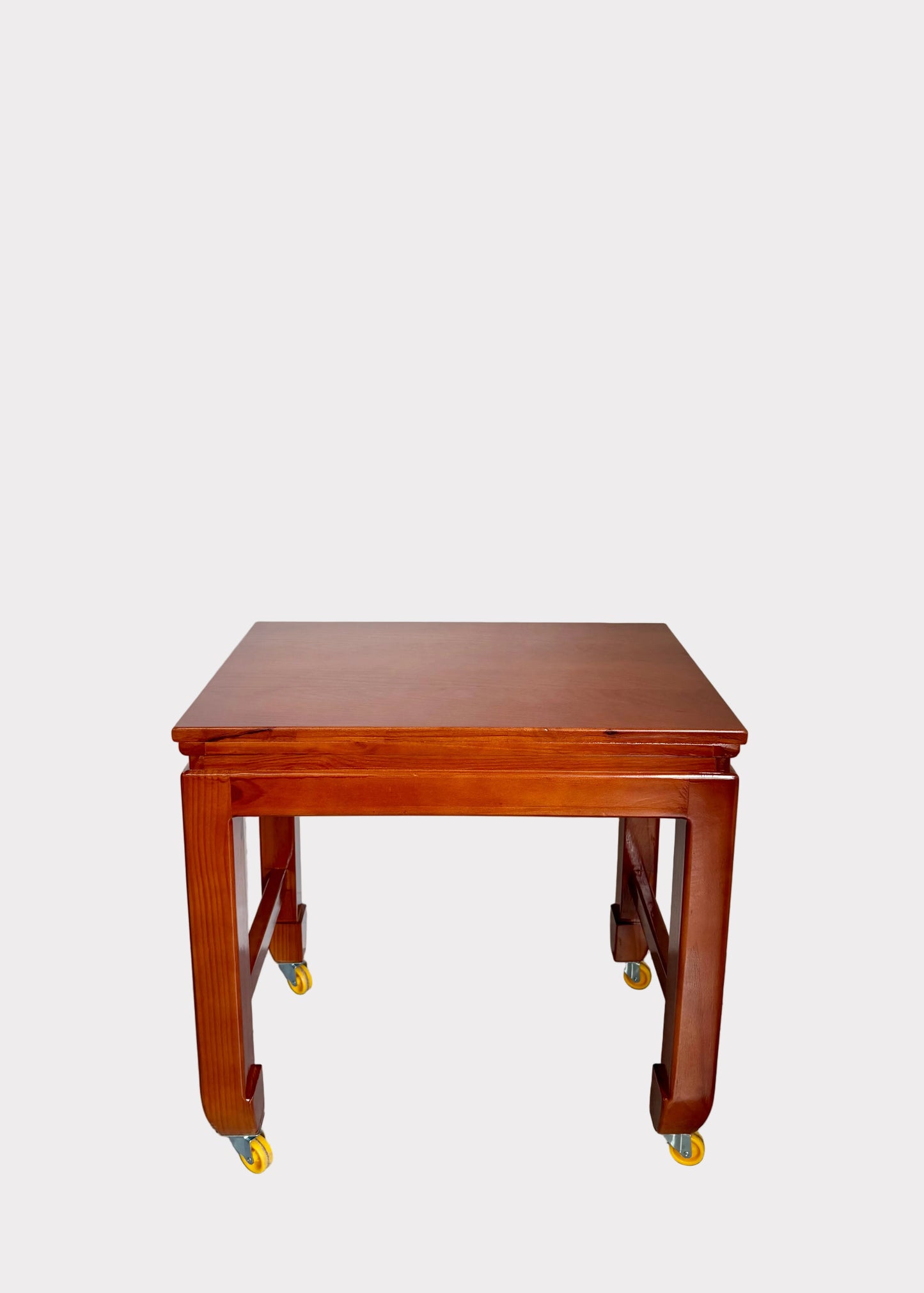A reddish-brown wooden table with casters, photographed against a plain off-white wall and gray speckled floor.