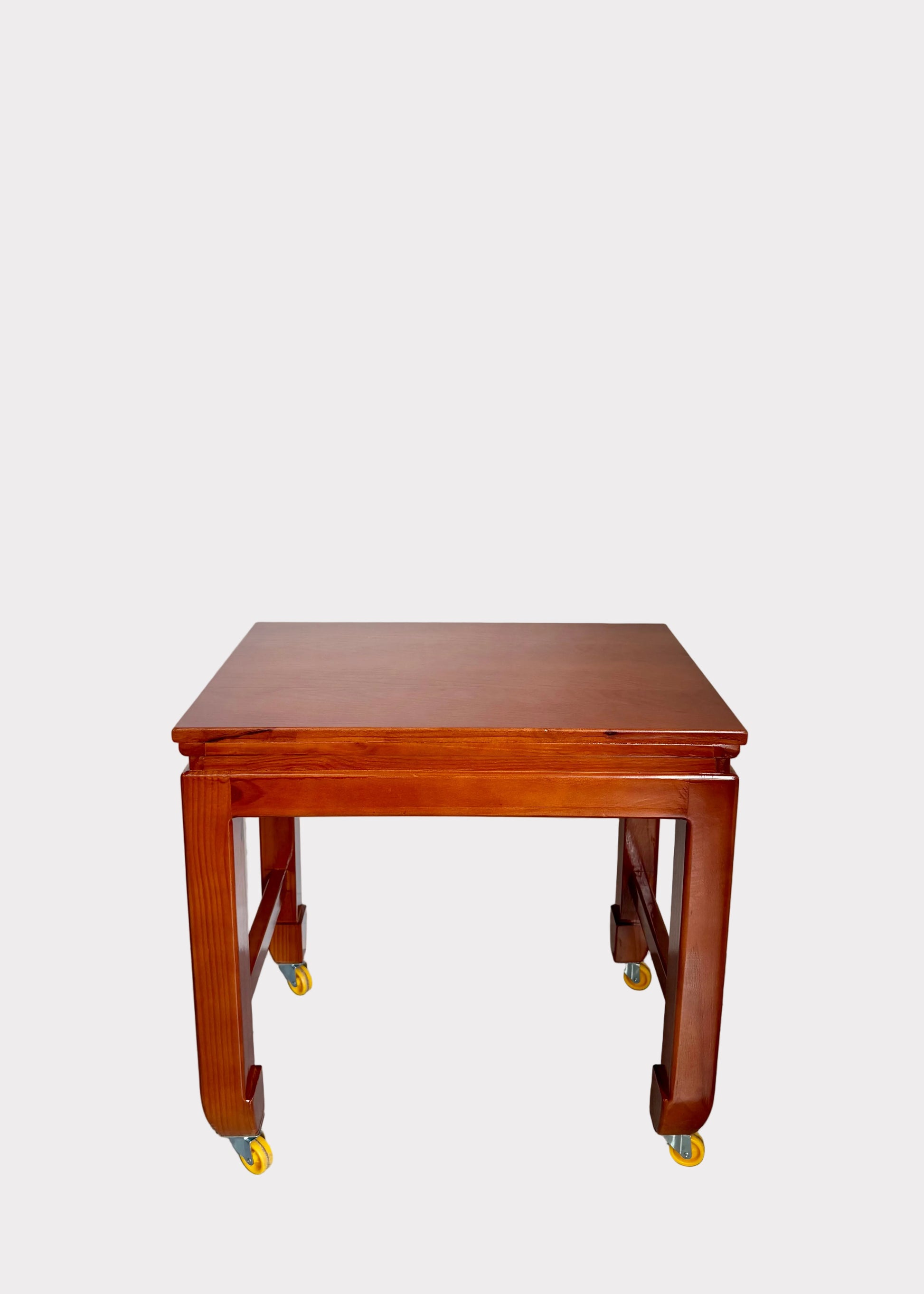 A reddish-brown wooden table with casters, photographed against a plain off-white wall and gray speckled floor.