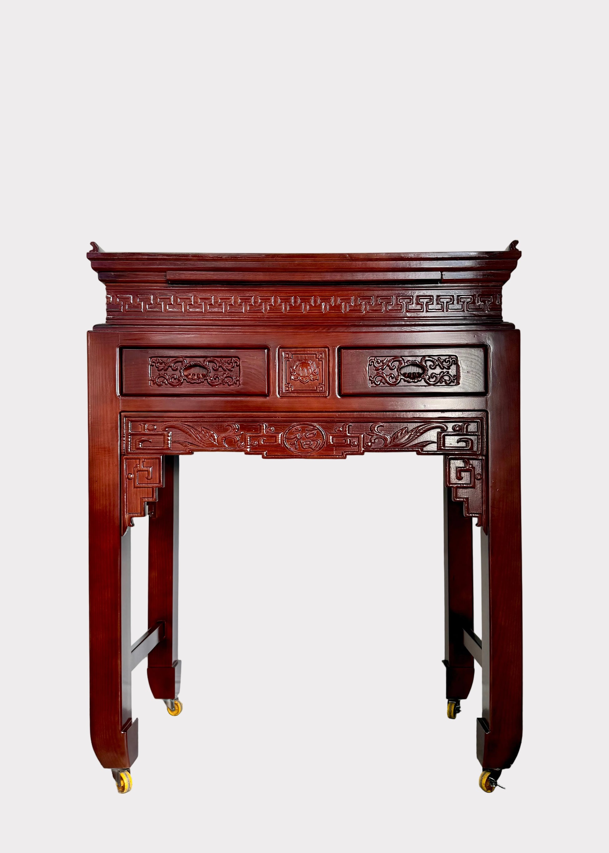 A traditional carved wooden console table with a reddish-brown finish and gold caster wheels, set against a plain white wall.