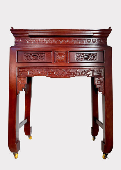 A traditional Chinese wooden console table or altar stand with intricate hand-carved details, featuring two drawers on the top, decorative brackets, and four legs on casters, shown in a room corner.
