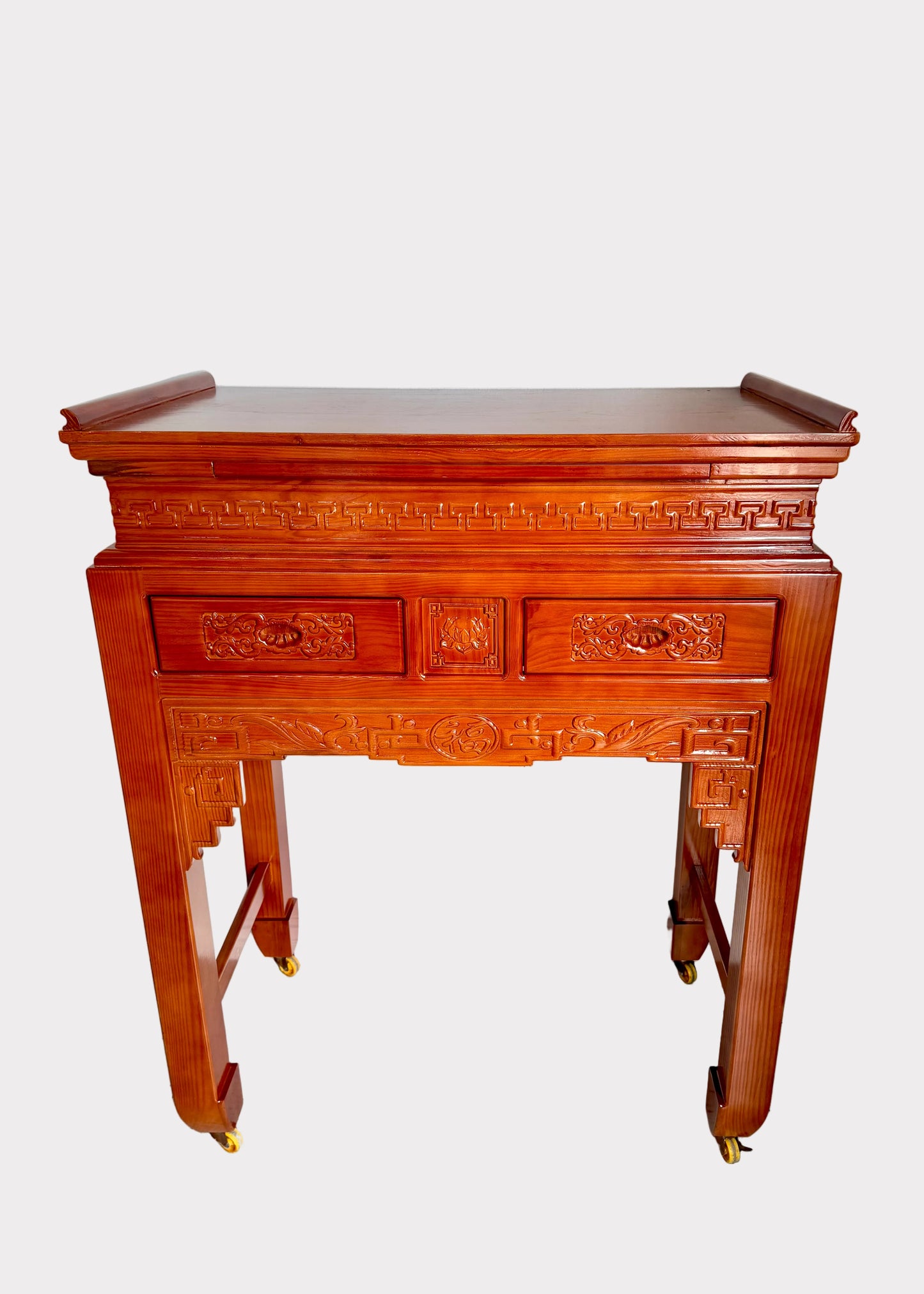 A traditional Chinese wooden console table with ornate carvings, two drawers, and four legs on small brass casters, shown against a plain white wall and gray speckled floor.