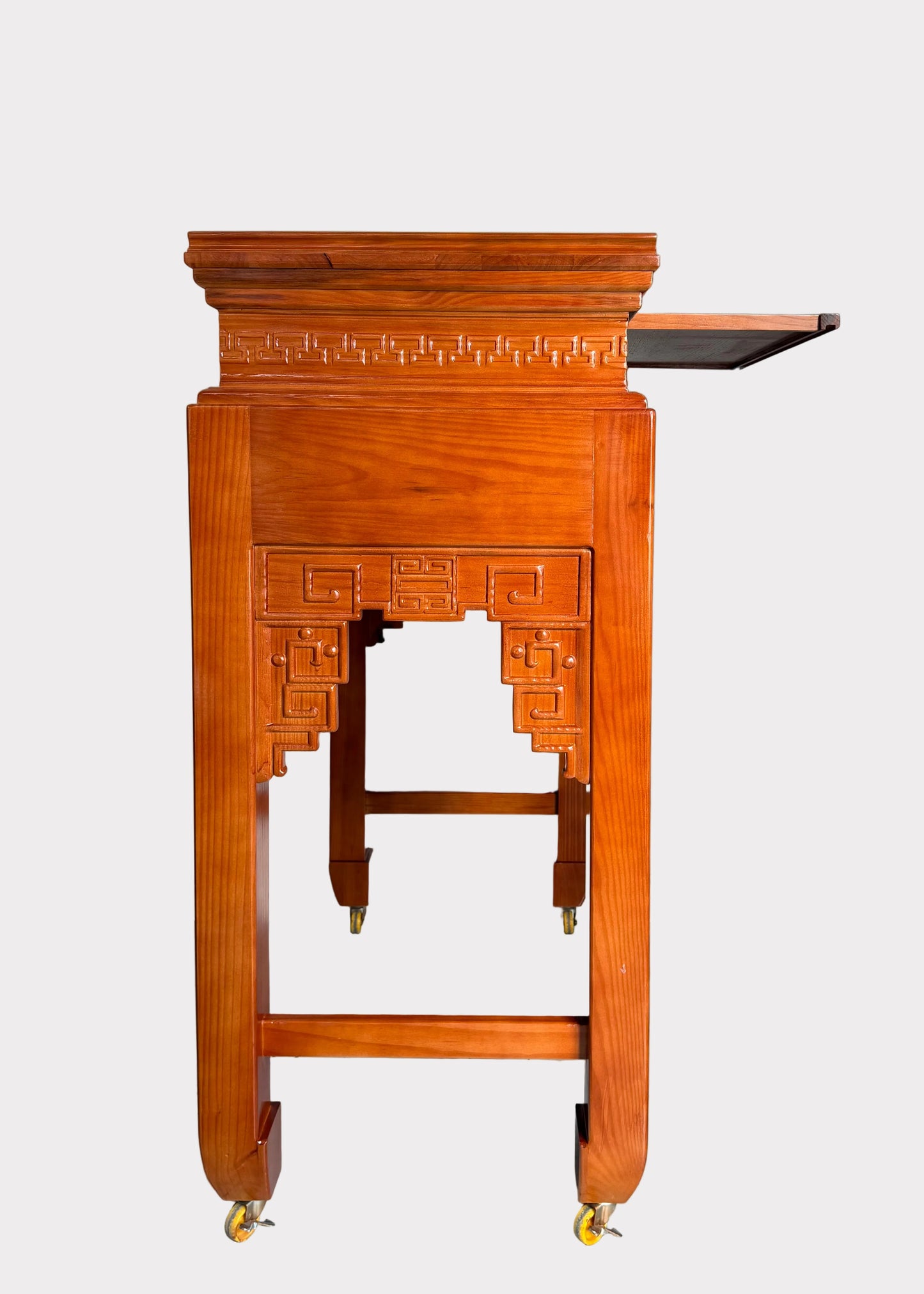 A traditional Chinese wooden display stand or lectern with ornate geometric carvings and four casters, shown against a plain light gray wall and speckled gray floor.
