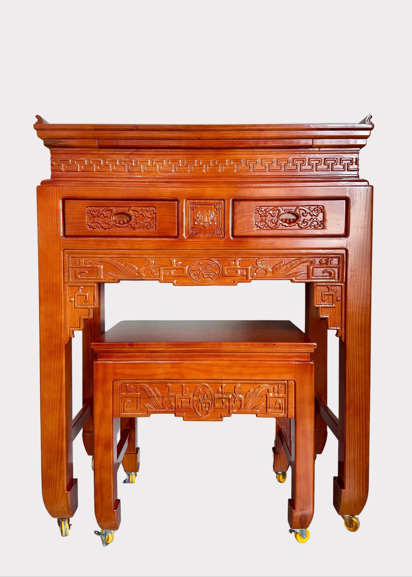 A traditional Chinese wooden writing desk and matching stool set with ornate carvings and brass caster wheels, photographed in a home interior setting.