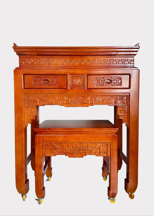 A traditional Chinese wooden writing desk and matching stool set with ornate carvings and brass caster wheels, photographed in a home interior setting.