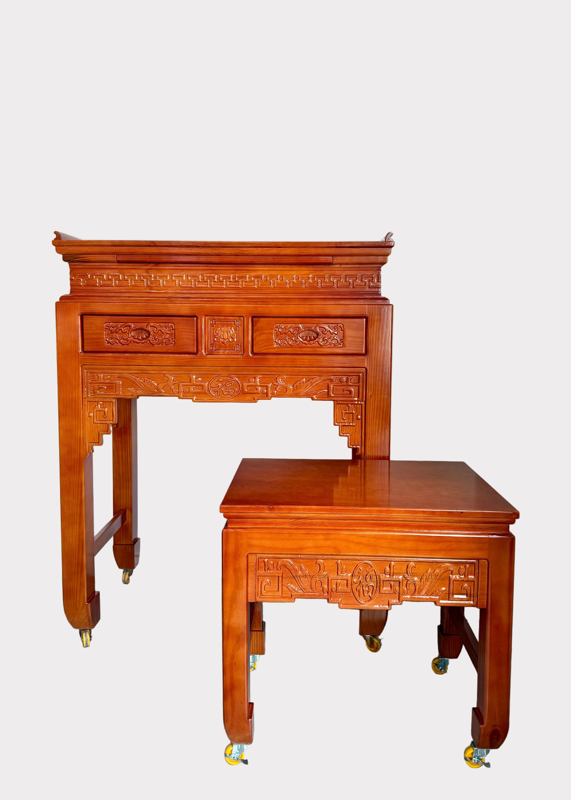 A traditional Chinese wooden writing desk with an attached matching storage cabinet, both featuring intricate carvings and brass caster wheels, set against a plain white wall and gray floor.