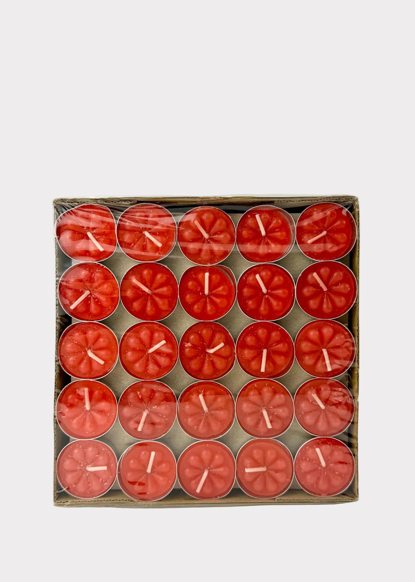 A boxed set of 20 red tea light candles arranged in a grid inside a clear plastic sleeve, photographed against a plain white wall and surface.