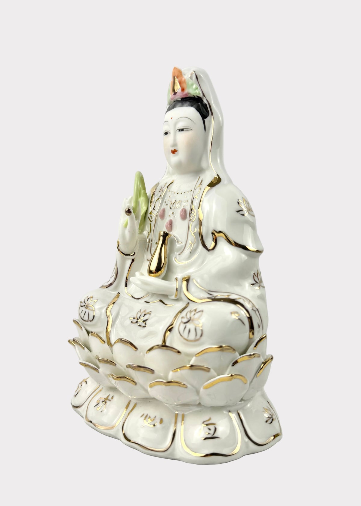 A white porcelain Guanyin statue seated on a lotus base, decorated with gold trim and small multicolor accents, photographed against a plain light gray background.