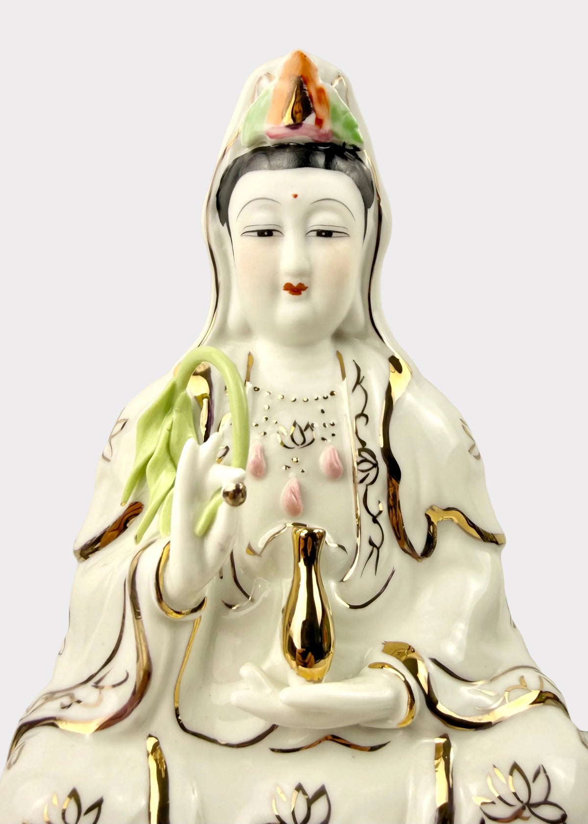 A white porcelain figurine of Guanyin, the Buddhist goddess of mercy, featuring gold-painted outlines and accents, pink and green details, and a lotus flower motif on her robes, set against a plain light gray background.