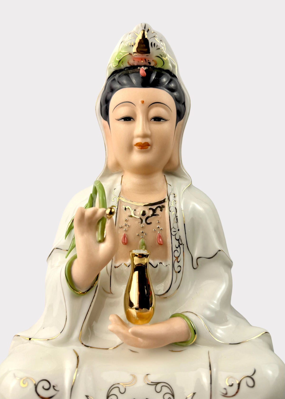 A white porcelain statue of Guanyin holding a gold bottle, featuring green and gold accents, set against a plain light gray background.