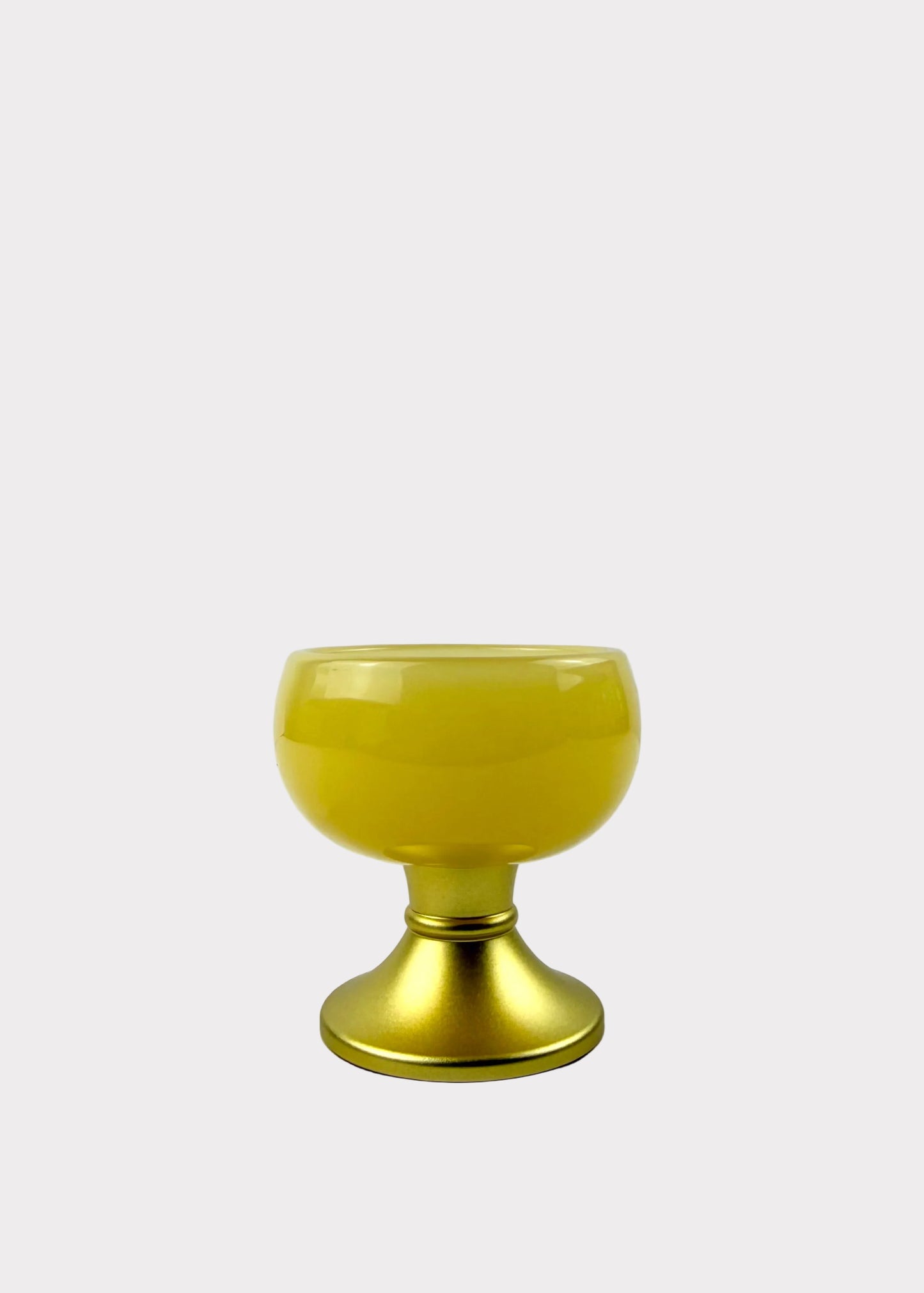 A small yellow glass goblet or candle holder with a metallic gold base, set against a light gray background.