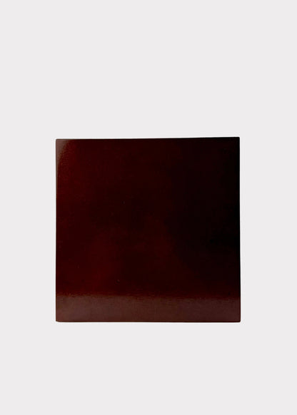 A square glossy dark red-brown color swatch card standing upright on a white surface against a white background.