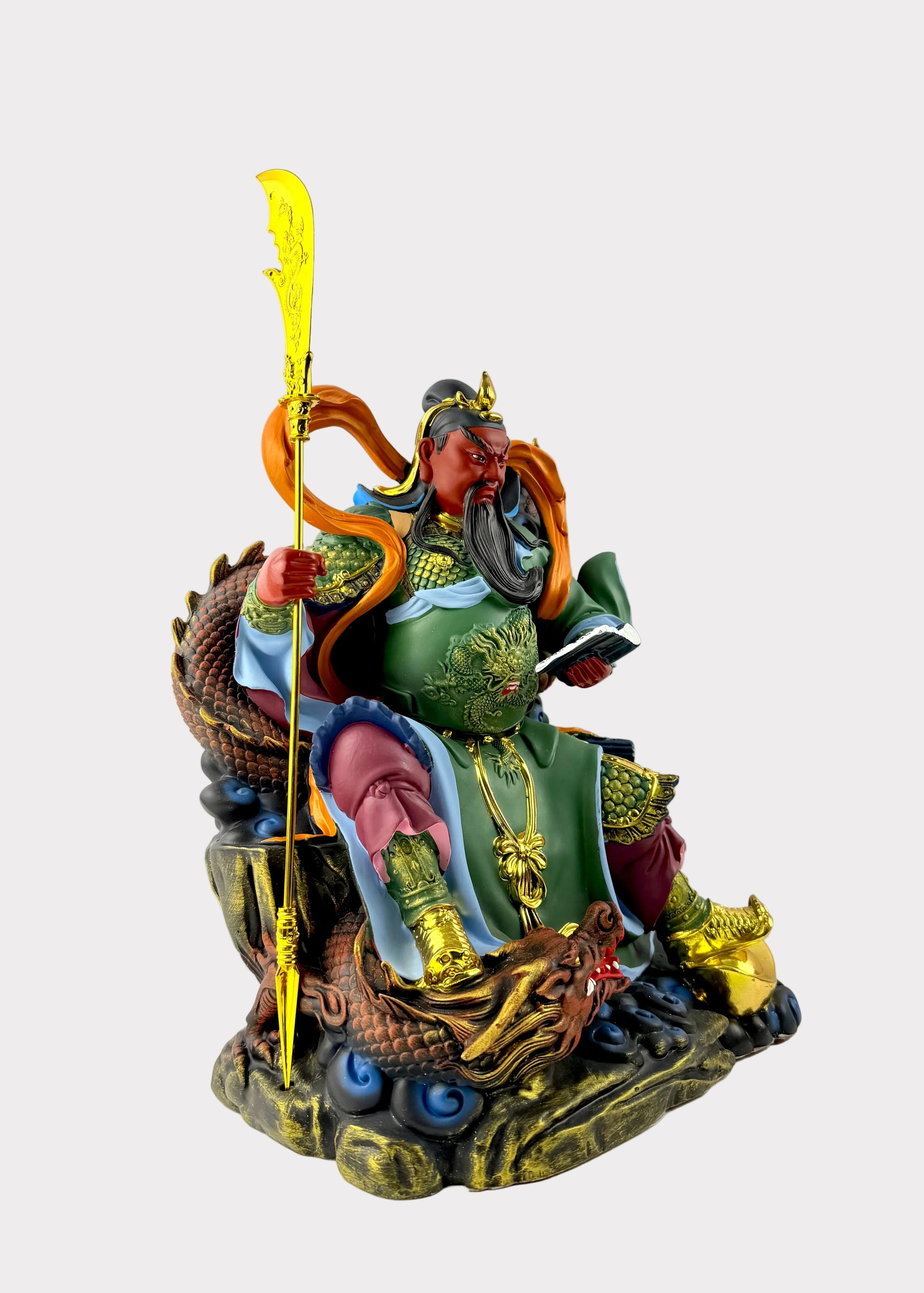 A colorful Chinese deity statue of Guan Yu seated on a dragon throne, holding a golden staff, photographed against a plain light gray background.