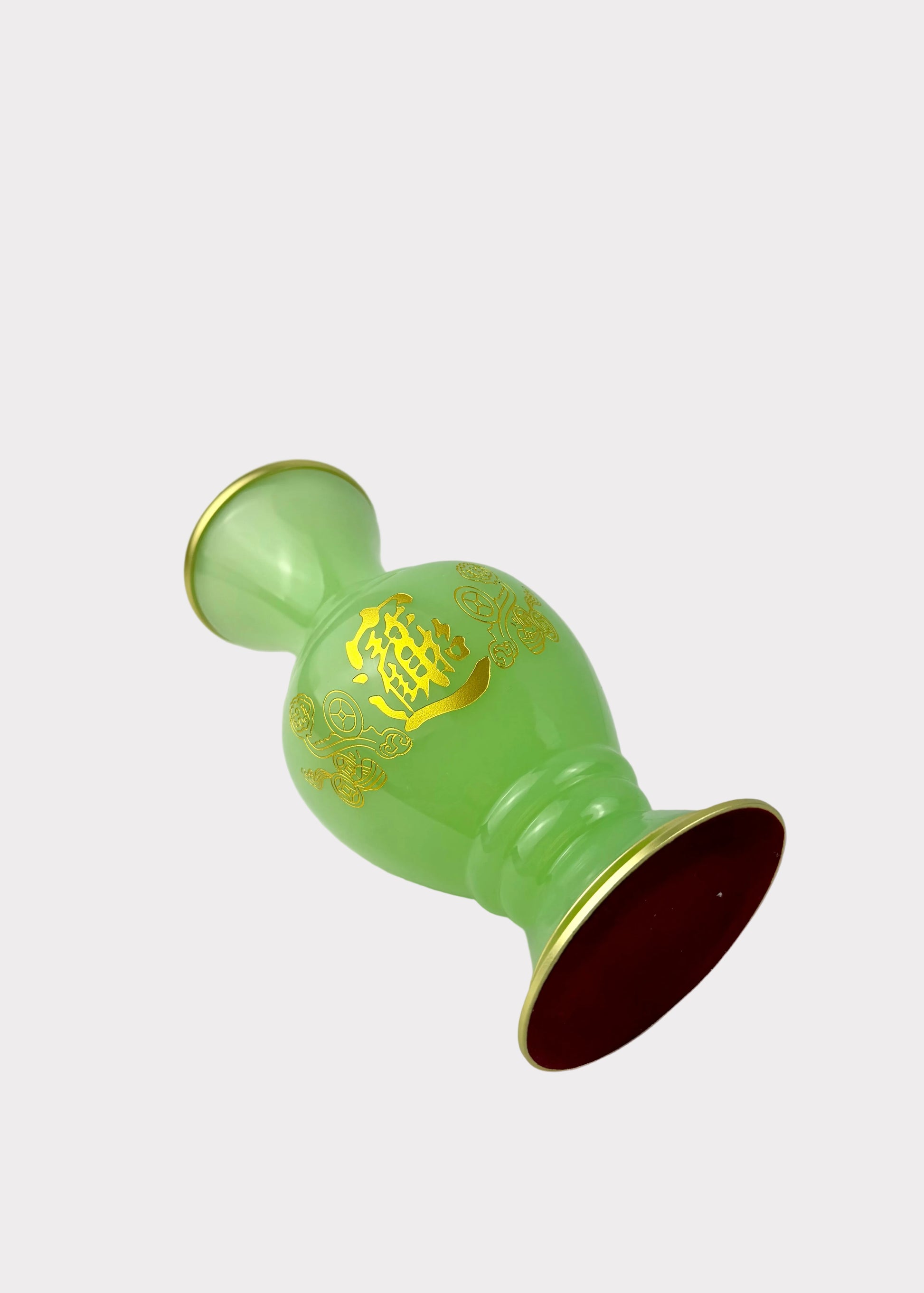 A light green glass vase with gold Chinese characters and floral patterns, featuring a gold-rimmed top and a dark red interior base, resting on a white surface.