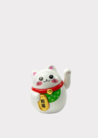 A white Japanese maneki-neko lucky cat figurine with a raised paw, wearing a red collar with a green scarf and a gold bell.