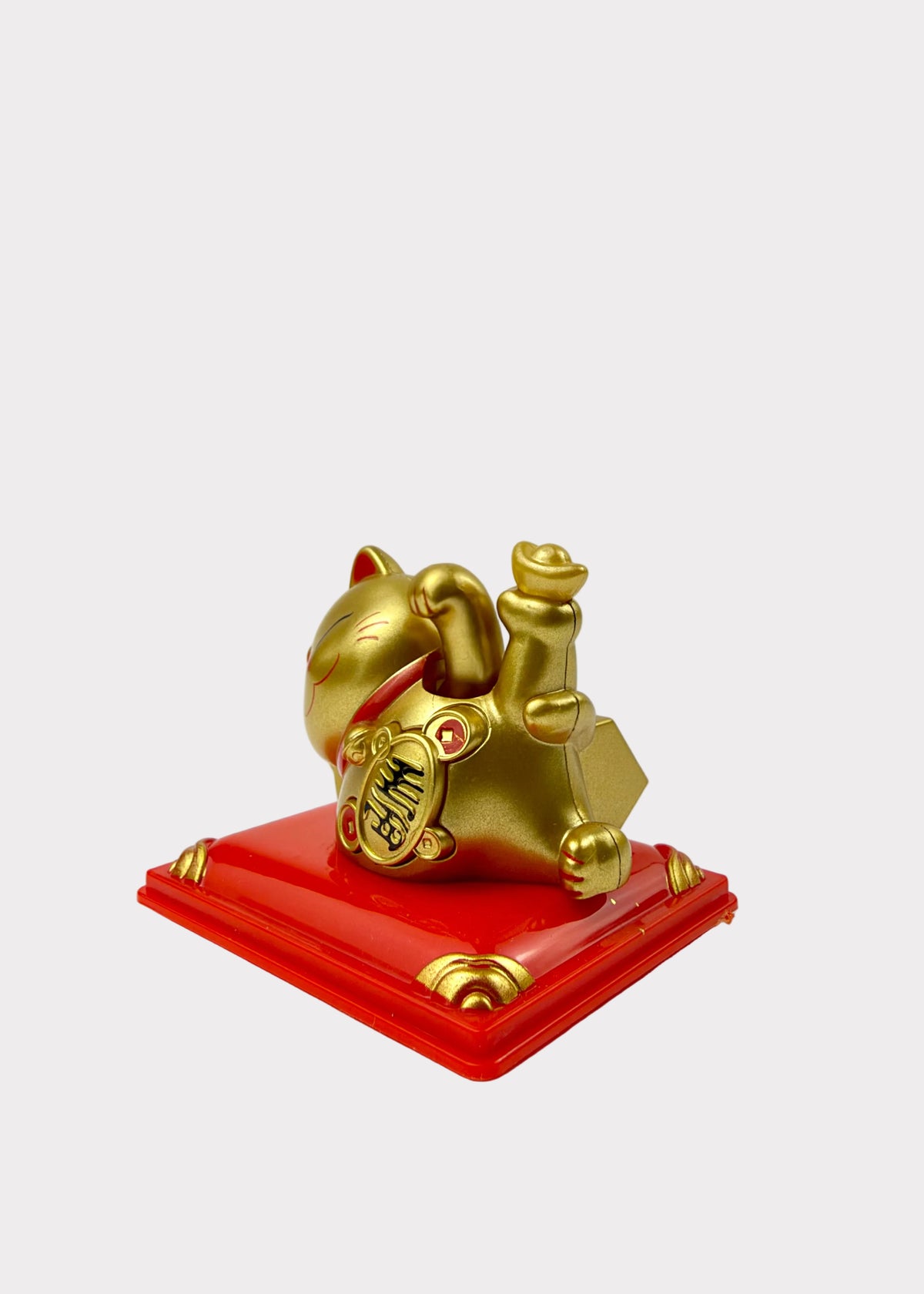 A golden maneki-neko lucky cat figurine holding gold ingots, resting on a glossy red square base with gold corner accents, photographed against a plain white background.