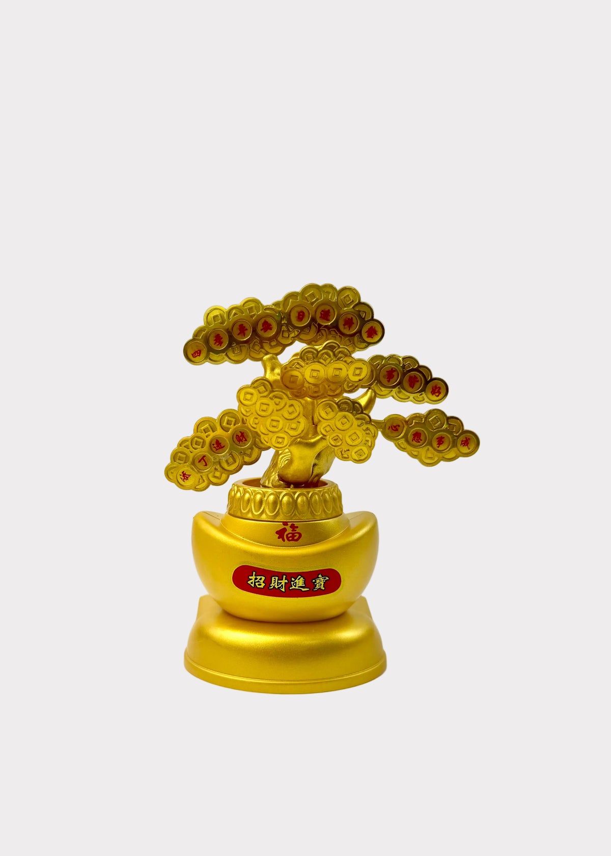A small golden decorative figurine shaped like a stylized tree with round gold leaves and red accents, mounted on a gold base with Chinese characters on a red label, photographed against a plain light background.