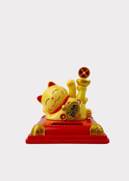 A yellow and red Japanese Maneki-neko lucky cat figurine sitting on a red base with gold accents, photographed against a plain white background.